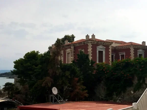 Historic architecture with red brick facade and lush greenery in Chalkis, overlooking the water. Tranquil and picturesque setting.