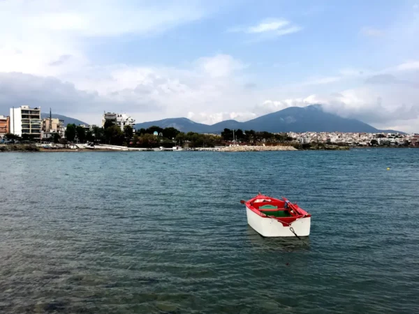 Colorful boat anchored in the clear waters of Chalkis, with mountains in the background and urban buildings along the shoreline.