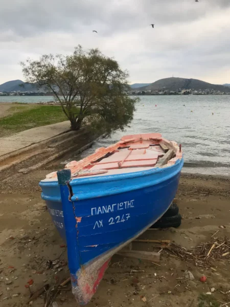 Bright blue fishing boat rests on the sandy shore, surrounded by calm water and distant hills, in Chalkis.