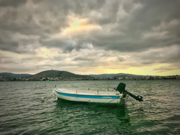 A tranquil boat floats on the waters near Chalkis, with dramatic clouds and a distant hill adding to the serene atmosphere.
