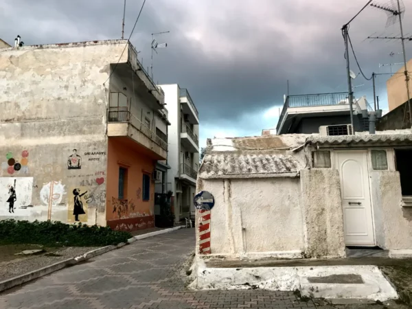 Chalkis showcases a narrow street lined with colorful graffiti, a whitewashed building, and dramatic cloud cover above.