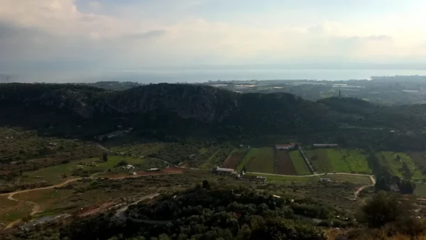 Vast green fields and rolling hills stretch across the landscape, with the shimmering waters of Chalkis visible in the distance.
