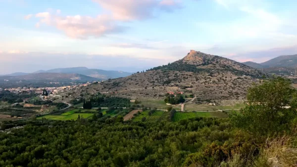 Picturesque landscape featuring rolling hills and lush greenery near Chalkis, with a distant hillside castle under a pastel sky.