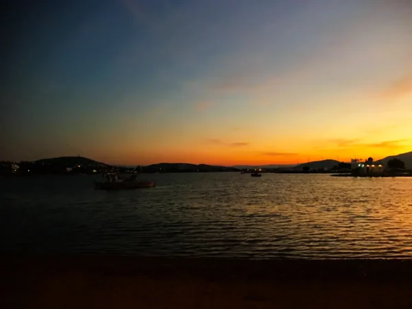 Tranquil sunset over the water in Chalkis, with boats silhouetted against vibrant orange and blue skies.