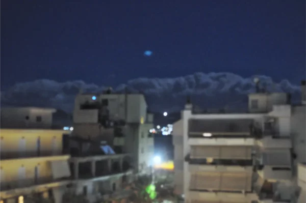 Nighttime view of Chalkis, Euboea, showcasing buildings under a starry sky with distant lights reflecting on water.