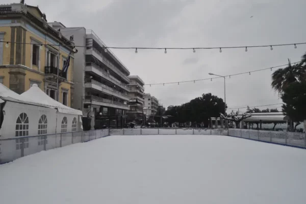 Ice rink adorned with string lights in Chalkis, Euboea, Greece, surrounded by cafes and colorful buildings.