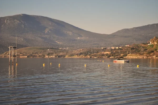 Tranquil waters reflect mountains near Chalkis, Euboea, Greece, with a boat gently floating among yellow buoys.