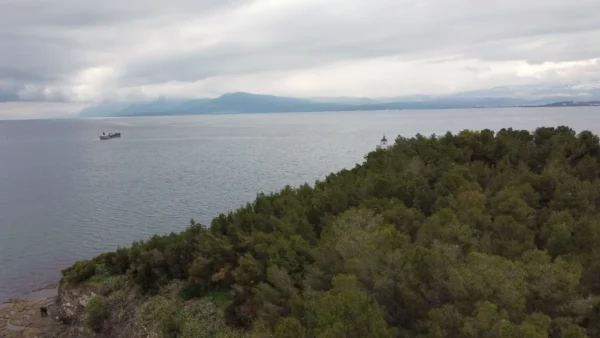 Calm waters of Chalkis, Euboea, Greece, framed by lush greenery and distant mountains under a cloudy sky.