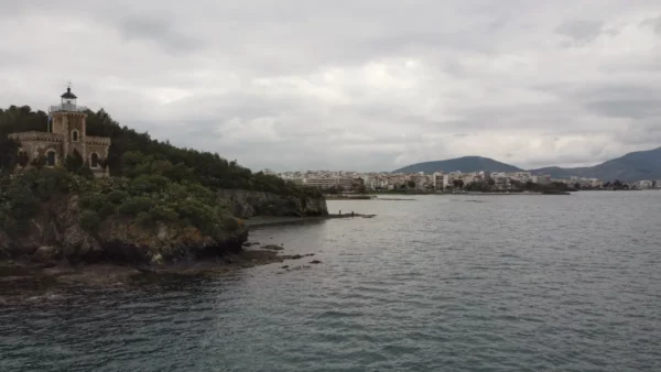 Historic lighthouse on a rocky shore, with the coastal town of Chalkis and mountains in the background, Euboea, Greece.