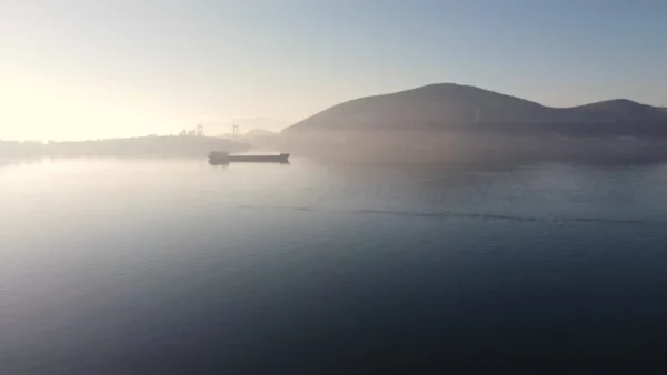 Calm waters reflect soft morning light, with a silhouette of a ship and distant hills in Chalkis, Euboea, Greece.