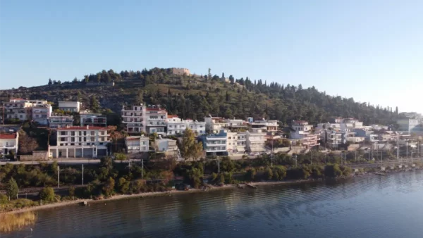 Chalkis showcases white buildings along the waterfront, nestled beneath a green hillside in Euboea, Greece, under clear skies.