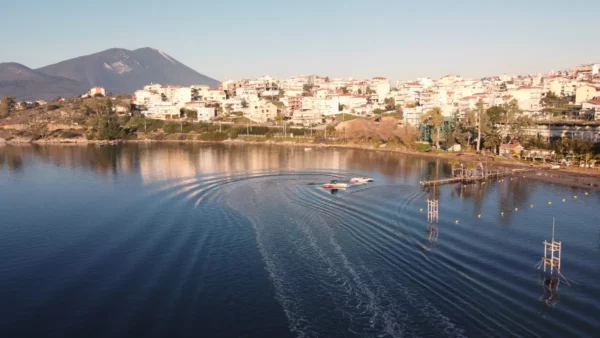 Chalkis features tranquil waters reflecting the city, with boats gently gliding along the surface against a backdrop of hills.