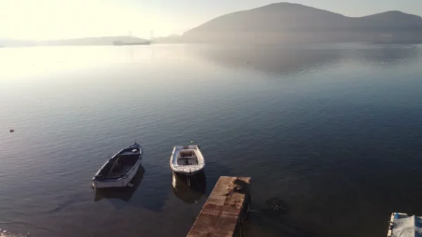 Serene waters reflect two boats and a distant hill in Chalkis, Euboea, Greece, under a soft morning light.