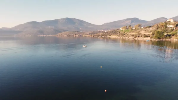 Calm waters reflect the soft hues of dawn near Chalkis, Euboea, Greece, with mountains framing the serene landscape.