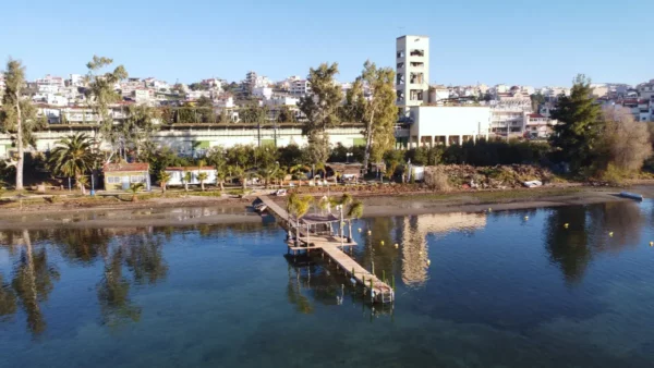 Serene waters reflect the pier and lush greenery along the shoreline in Chalkis, Euboea, Greece, showcasing vibrant coastal life.