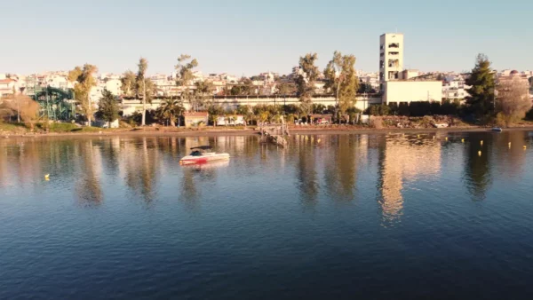 Chalkis features a tranquil waterfront with a small boat on the water, surrounded by lush trees and distant buildings in Euboea, Greece.