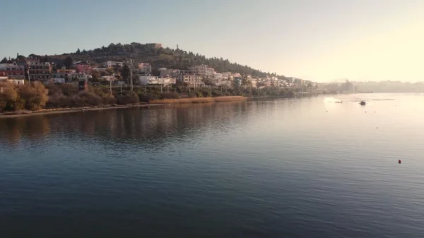 Calm waters reflect the hillside homes of Chalkis, Euboea, Greece, under a serene morning light along the shoreline.