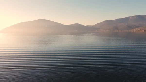 Calm water ripples reflect the soft hues of dawn, framed by the misty hills surrounding Chalkis, Euboea, Greece.