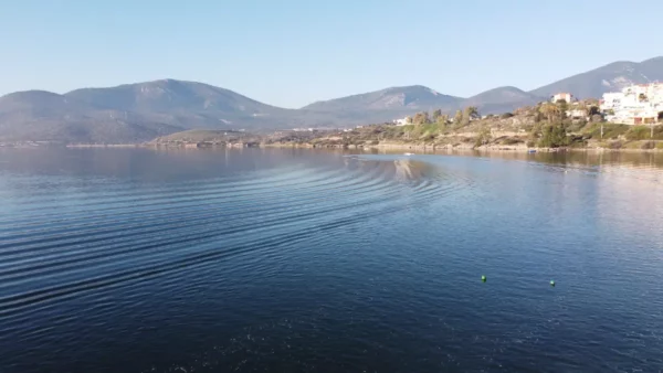 Gentle ripples in the water reflect the serene landscape of Chalkis, Euboea, showcasing mountains and coastal greenery.