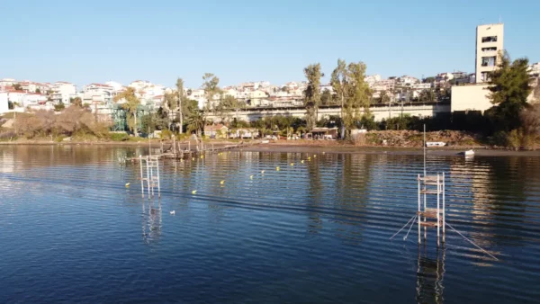 Scenic view of Chalkis, Euboea, featuring calm waters, reflections, and fishing platforms against a backdrop of city buildings.