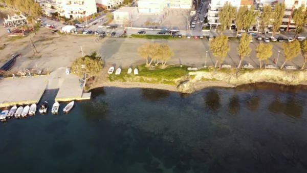 Chalkis features a tranquil waterfront with boats lined up, clear waters, and trees casting shadows on the shore in Euboea, Greece.