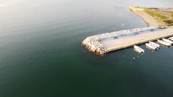 Chalkis features a serene pier with fishing boats, surrounded by calm waters and rocky shorelines under a clear sky.