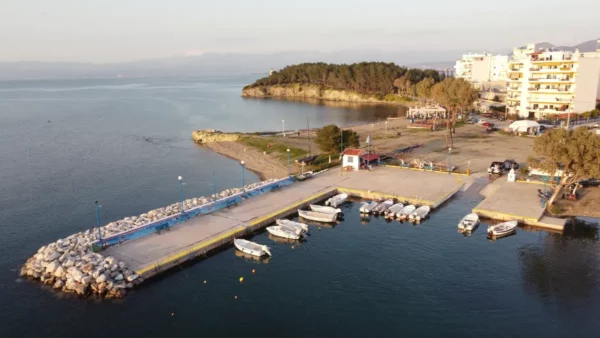 Charming harbor in Chalkis, Euboea, features fishing boats docked by a quay, with lush greenery and calm waters in the background.