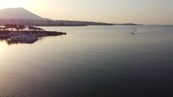 Calm waters reflect the sunset over Chalkis, Euboea, with hills in the background and a boat gently cruising along.