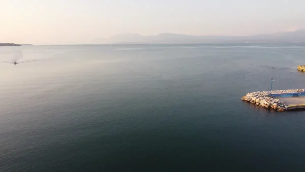 Serene waters reflect the soft hues of sunset near Chalkis, Euboea, Greece, with a rocky pier extending into the calm sea.