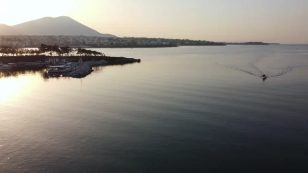 Gentle waves reflect the soft evening light of Chalkis, Euboea, with a distant mountain backdrop and a boat gliding across the water.