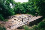 Ruins of an ancient Greek Doric temple at Kardaki, Mon Repos Park, Corfu Town, Greece, with stone foundations surrounded by trees and grass.