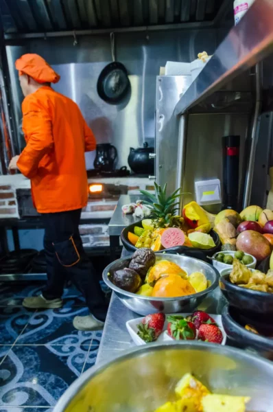 Cooking-class in a Salento, Colombia kitchen with a cook in an orange apron and bowls of fresh fruits.