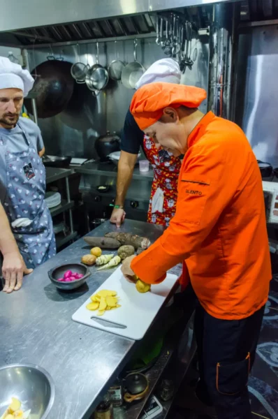 Cooking class in Salento, Colombia: chef in orange chops vegetables in a busy kitchen.
